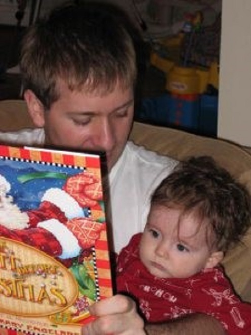 A dad and 6 month old baby reading a book.