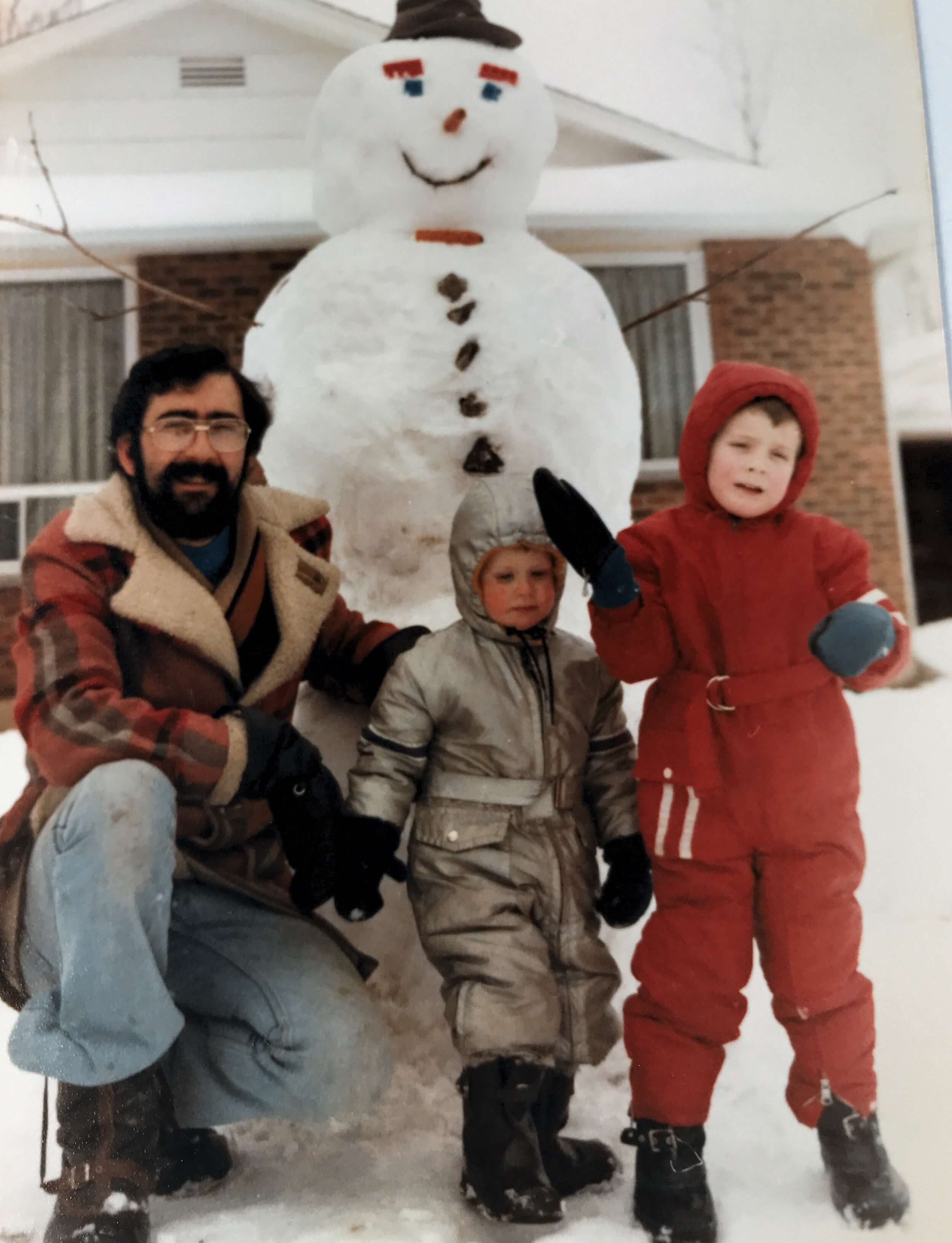 two boys and a dad building a tall snowman