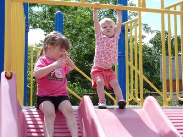 A 2 year old playing with her sister on the slide.